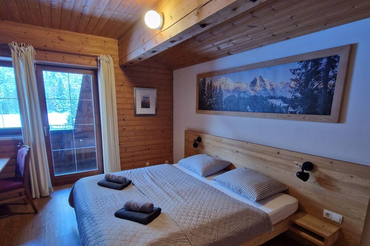 Une chambre dans une cabane en bois, avec un grand lit, un tableau au mur et une fenêtre avec des rideaux.