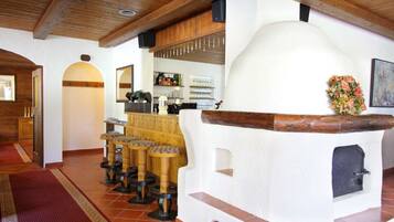A rustic interior with a stone oven, wooden stools, and a bar area.