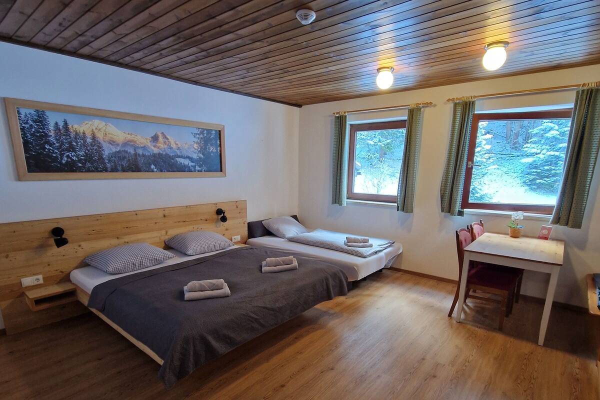 Une chambre confortable avec un plafond en bois, un grand lit, deux petits lits, un bureau et une fenêtre avec des rideaux.