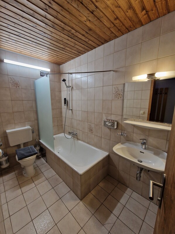 A bathroom with a wooden ceiling, a bathtub, a toilet, and a sink.