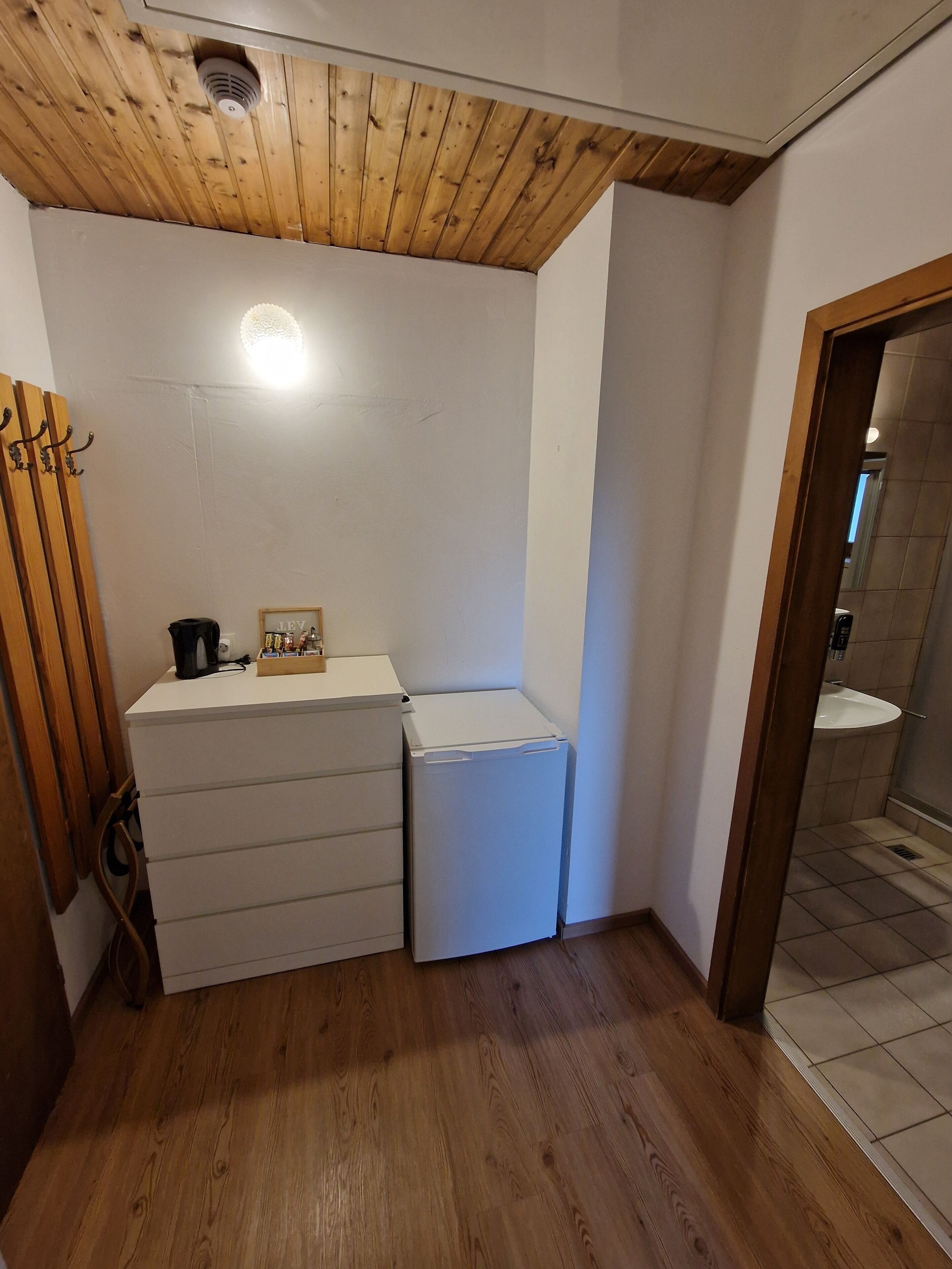 Un baño pequeño con techo de madera, un lavamanos blanco y una lavadora compacta.
