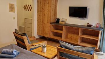 A cozy room with a bed, wooden furniture, a TV, and a small table with a kettle.