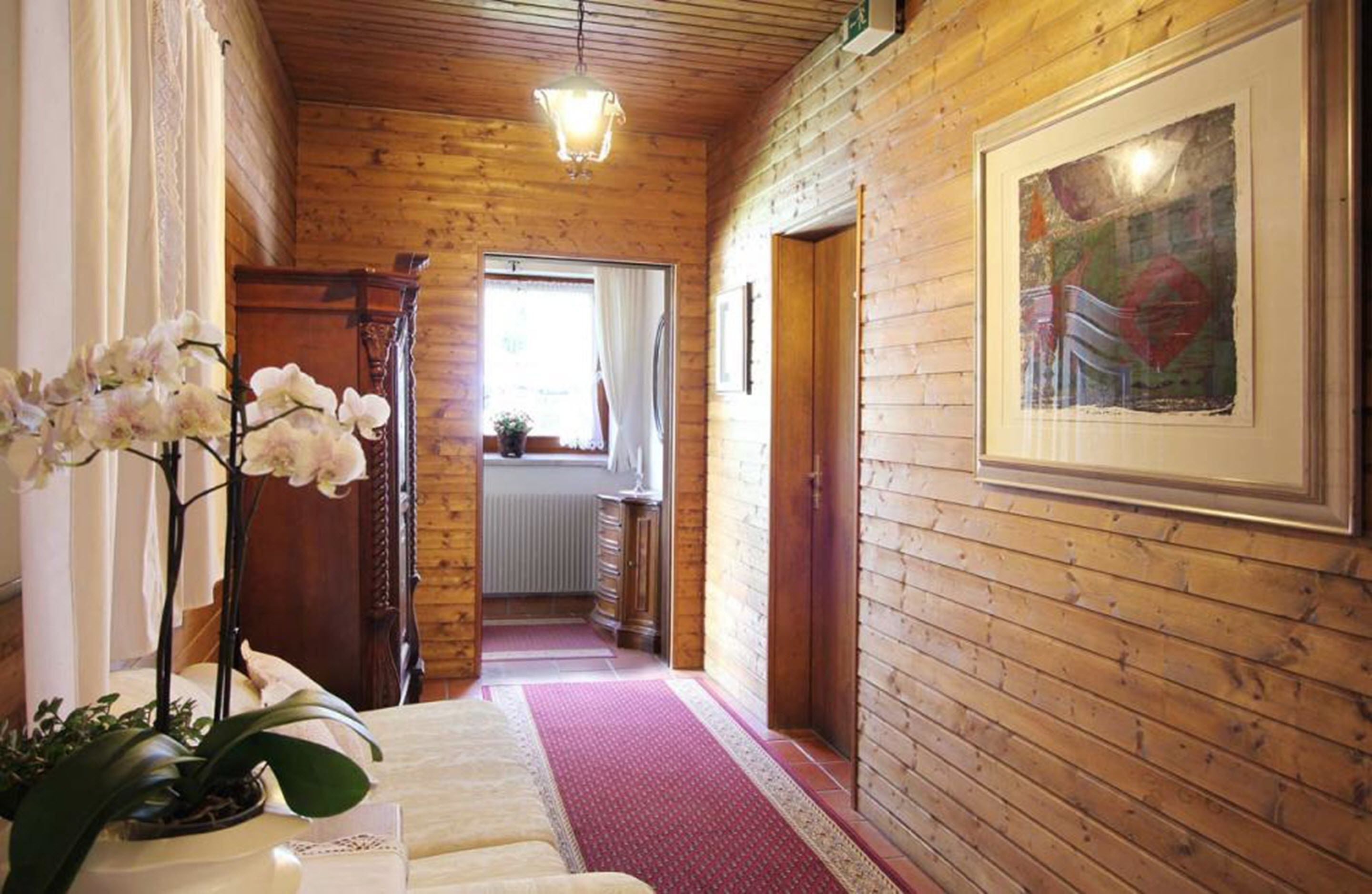 Un pasillo interior de madera con un radiador, un cuadro enmarcado y una orquídea en maceta.