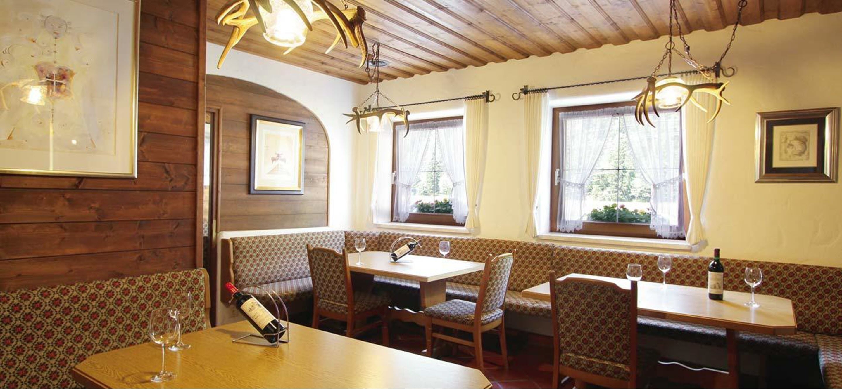 A cozy restaurant with wooden walls, patterned benches, and tables with wine glasses and bottles.