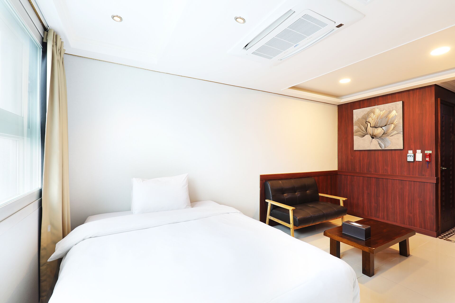 Una habitación de hotel con una cama, una mesita de madera, un sillón de cuero y un armario de madera.