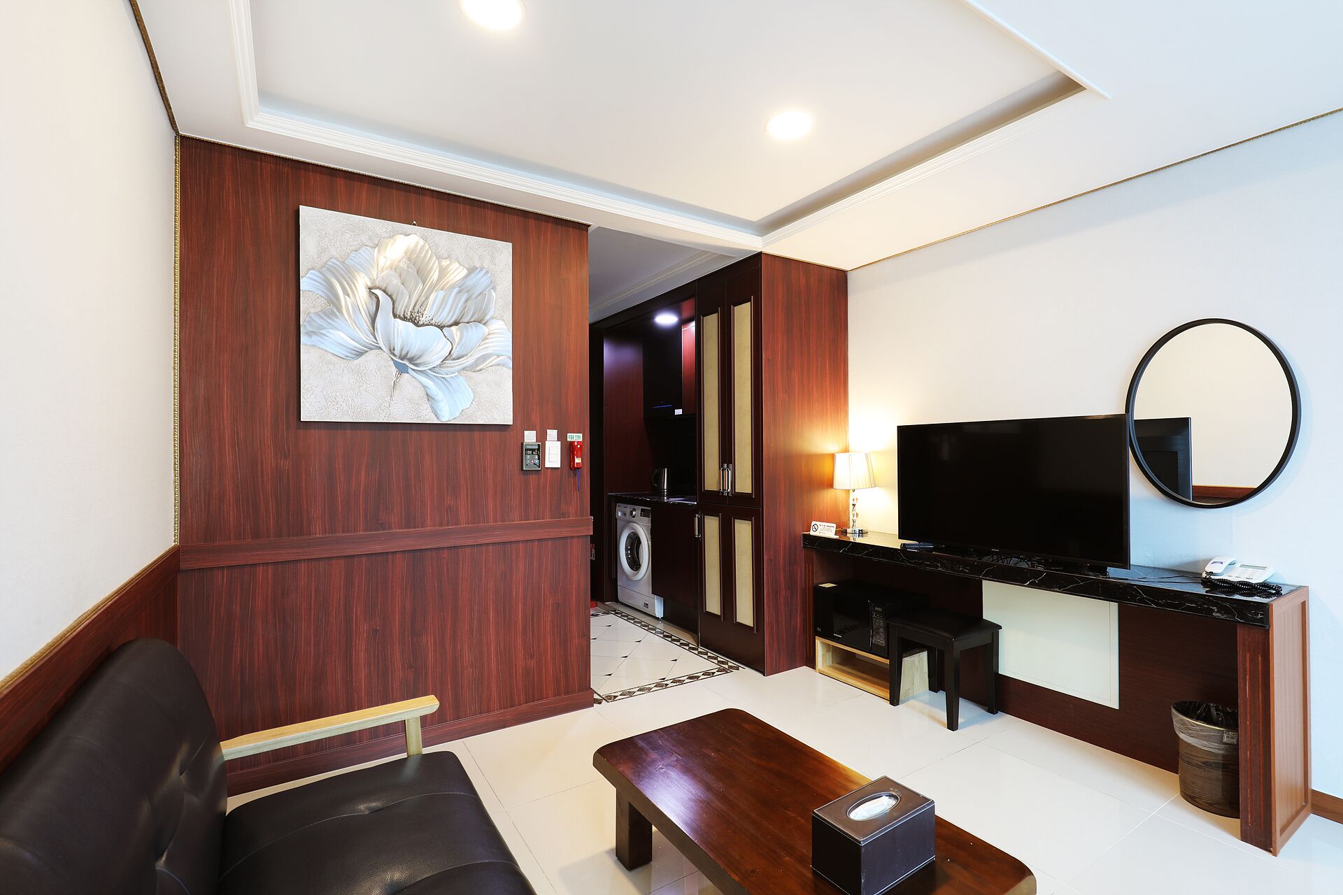 Une chambre d’hôtel équipée d’un canapé, d’une table basse, d’une télévision, d’un miroir, d’un tableau et d’une petite kitchenette.