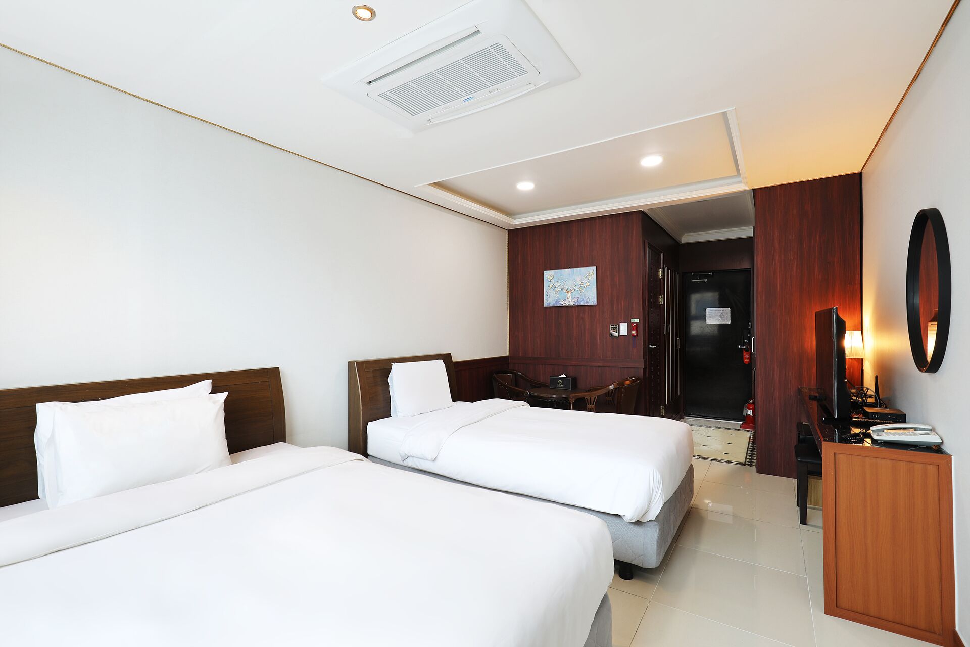 A hotel room with two beds, a desk, a chair, a mirror, and a door leading to a bathroom.
