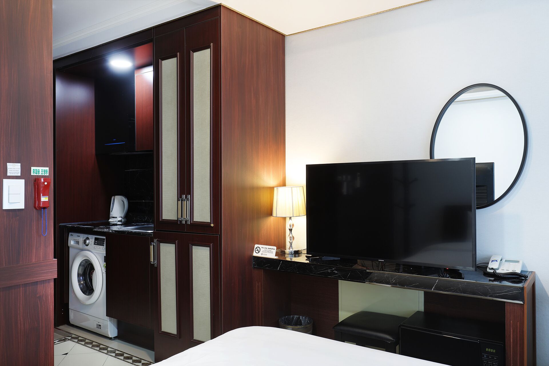Habitación de hotel con lavadora, televisión, escritorio con lámpara y un espejo en la pared.