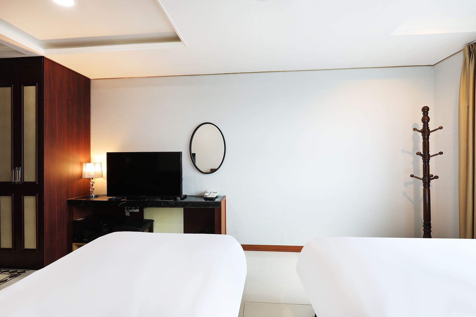 A hotel room with two beds, a TV, a mirror, and a coat rack.