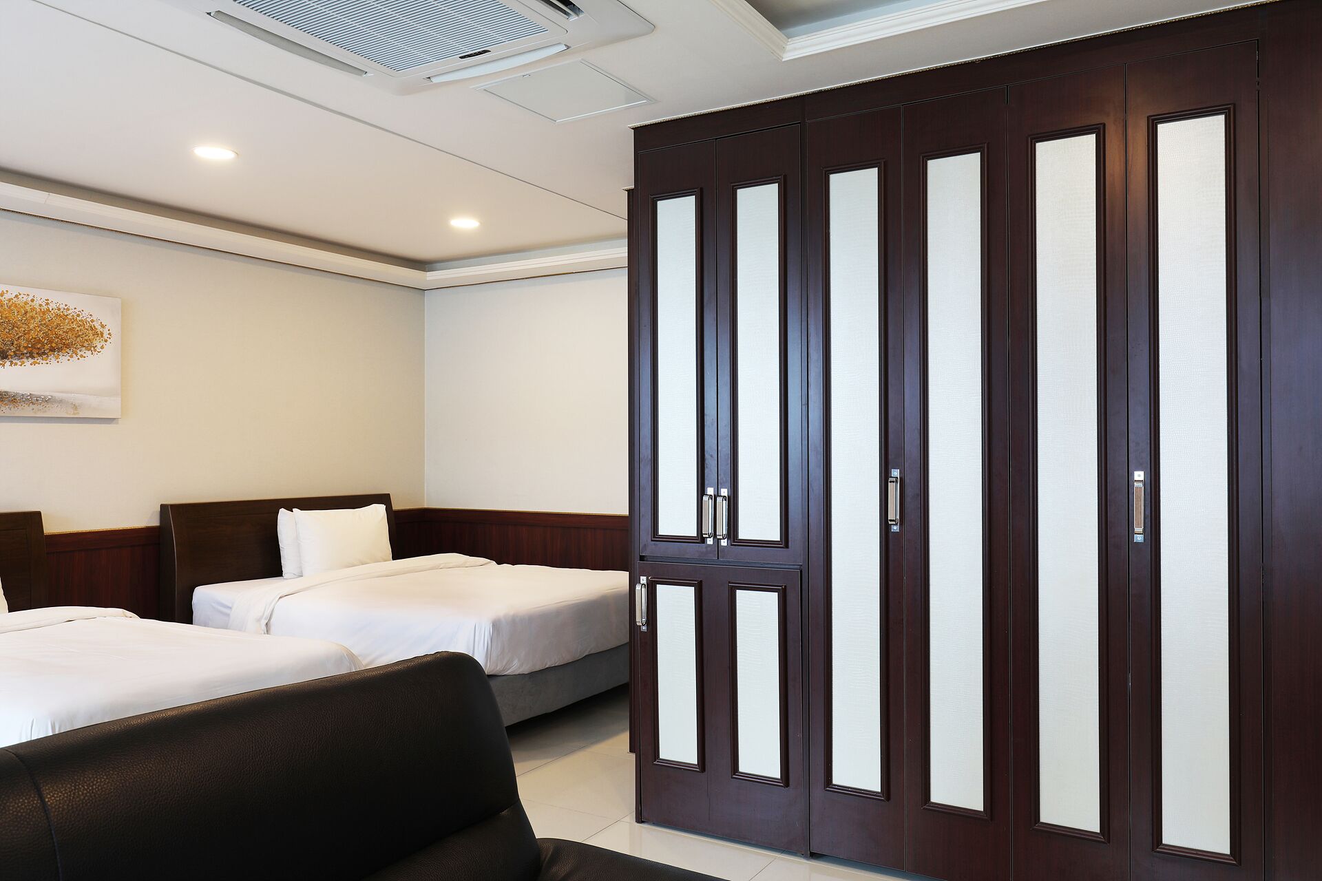 Habitación de hotel con dos camas, un armario de madera oscura y una rejilla de ventilación en el techo.