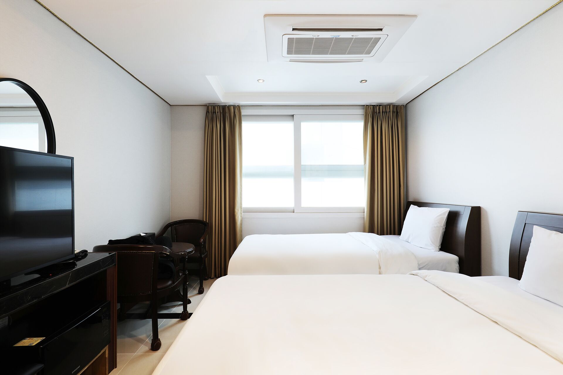 A hotel room with a bed, a desk with a television, a chair, and a window with curtains.