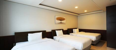 A hotel room with three single beds, a ceiling with recessed lighting, and a wall-mounted artwork of a tree.