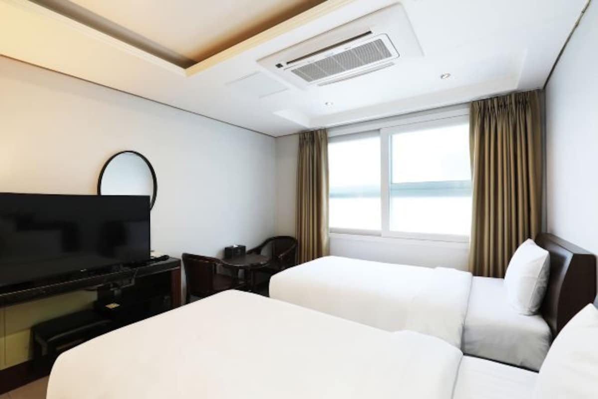 Habitación de hotel con dos camas, televisión, escritorio y ventana con cortinas.