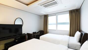 A hotel room with two beds, a TV, a desk, and a window with curtains.