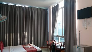 Hotelkamer met een bed, een stoel, een bureau, een televisie en een raam met gordijnen.