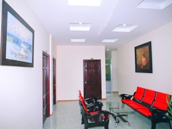 A hallway with a red sofa, a glass table, and two chairs. There are framed pictures on the walls and a door at the end.
