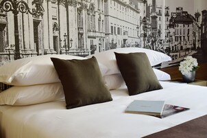 A neatly made bed with white linens and two dark pillows, a book on the bed, and a vase with flowers on the nightstand.