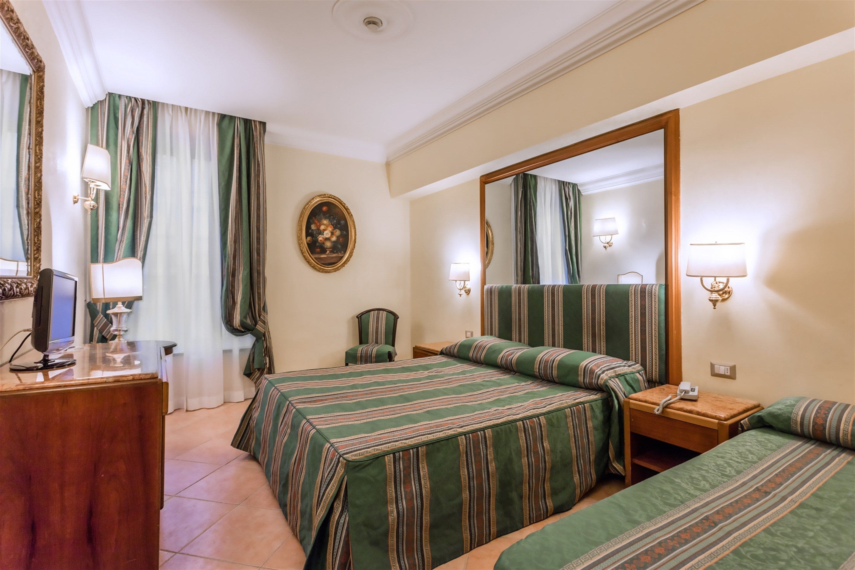 A hotel room with two beds, a desk, a chair, a mirror, and a painting on the wall.