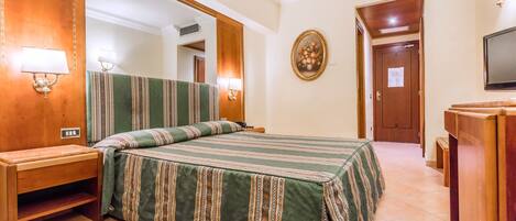A hotel room with a large bed, wooden headboard, bedside tables, a mirror, a television, and a door with a sign.