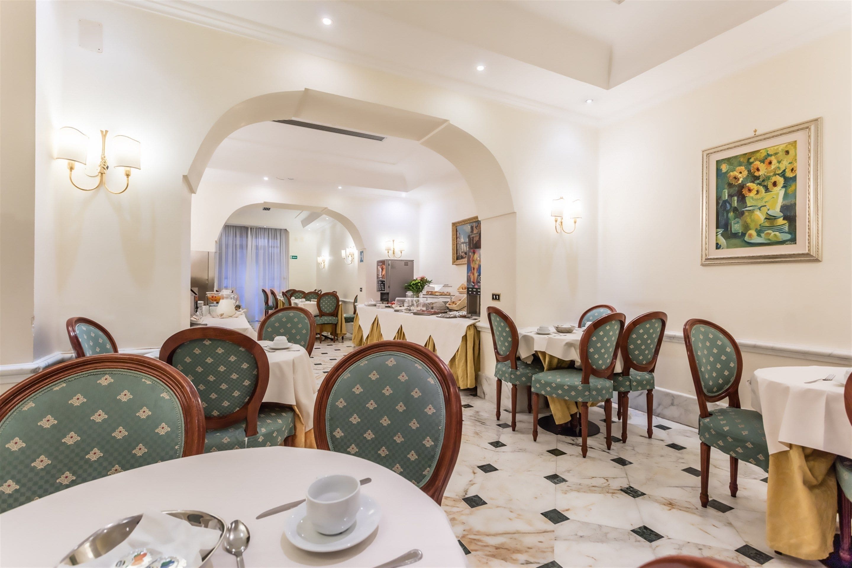A dining area with round tables, green upholstered chairs, and a marble floor.