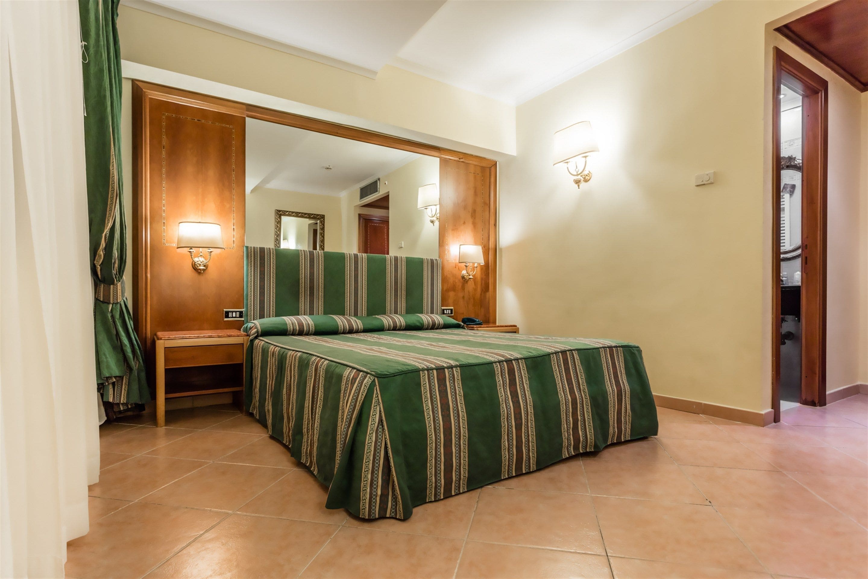 A hotel room with a bed, a nightstand, a mirror, and a door leading to a hallway.