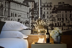 Et hotelværelse med en seng, et natbord med vin og glas, samt et vægmaleri af et bybillede.