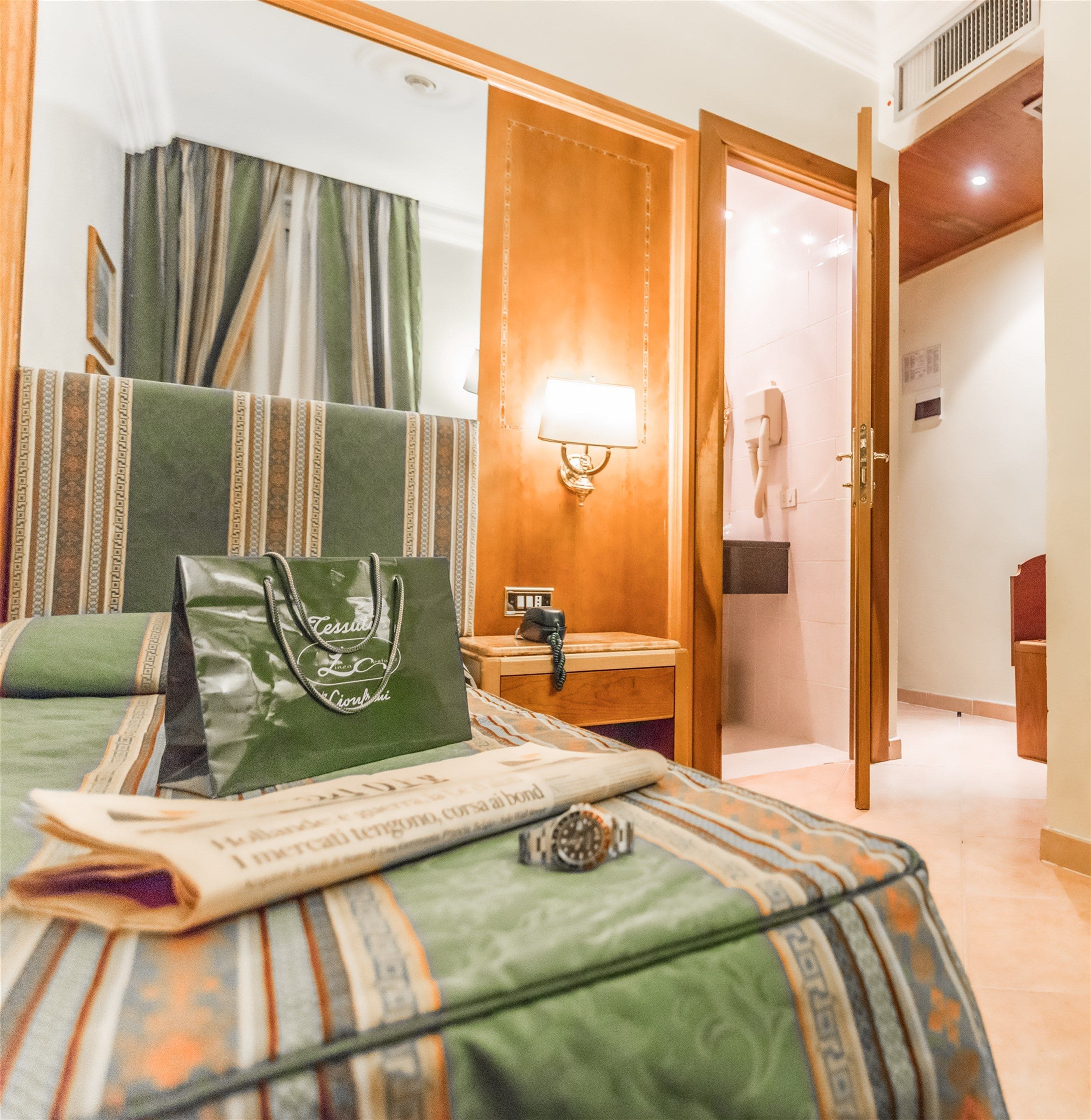 Una habitación de hotel con cama, mesita de noche, lámpara, teléfono y puerta.