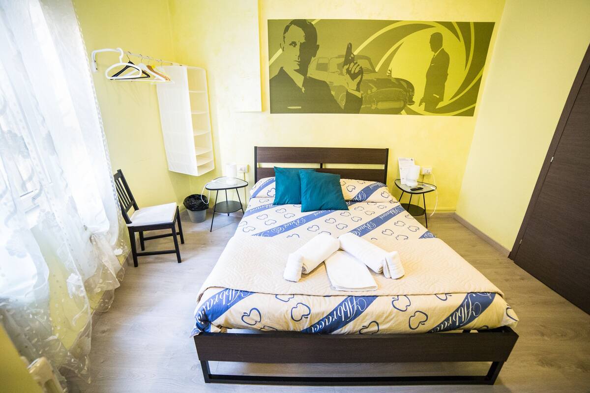 A hotel room with a bed, a chair, a small table, and a wall with a painting.