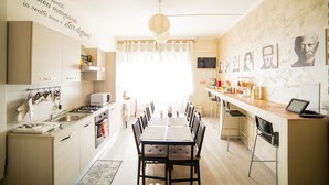 A modern kitchen with a dining area, featuring a long table, chairs, and a kitchen counter with appliances. - Movie Home B&B (Rome)