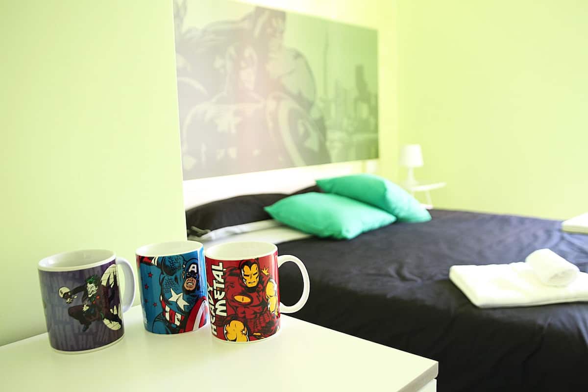 A hotel room with a bed, green walls, and three mugs on a table.