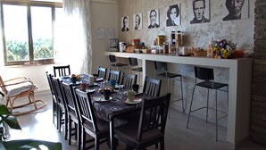A dining area with a long table set for multiple people, chairs, a kitchen counter with various items, and a window with curtains. - Movie Home B&B (Rome)