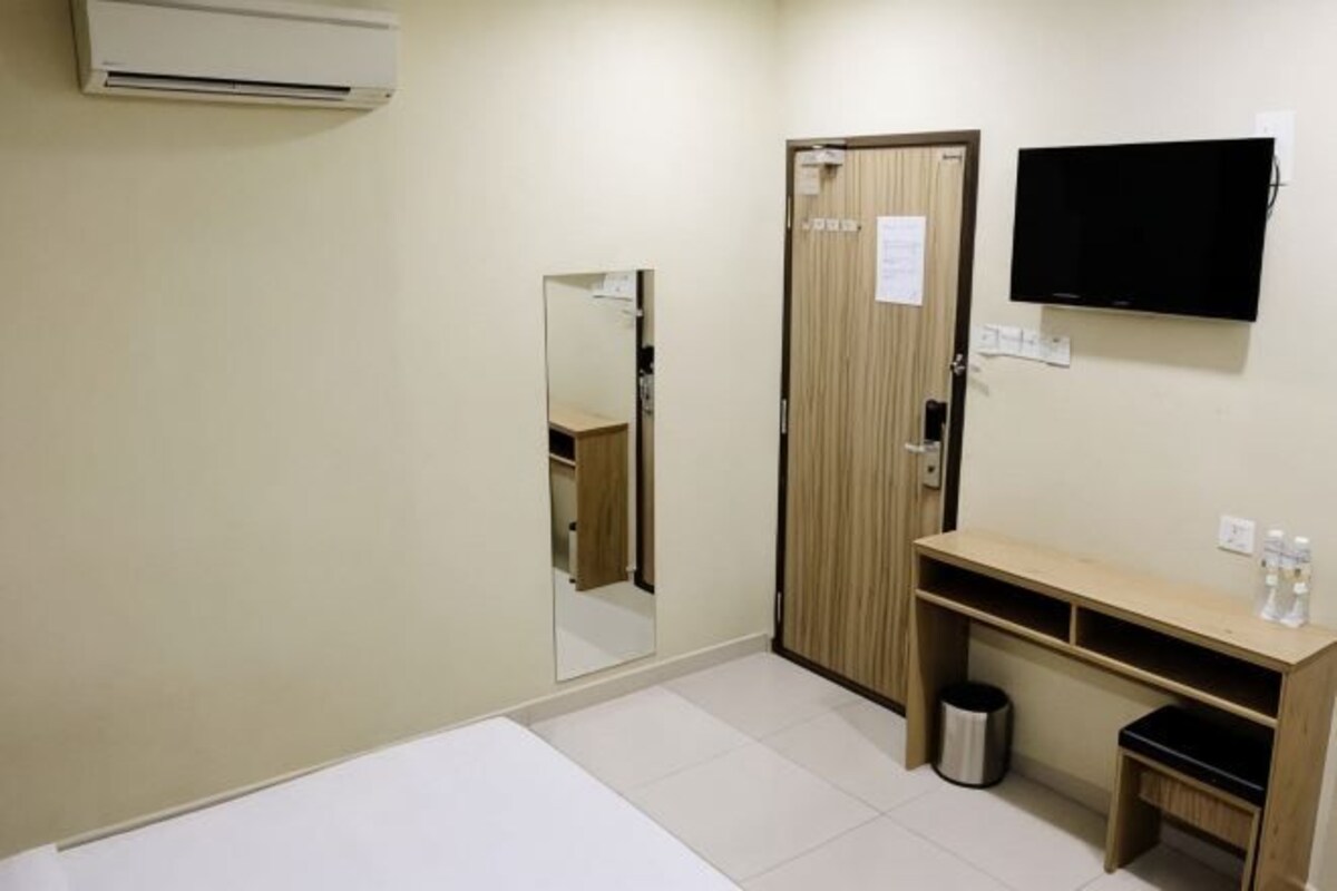 Camera d'albergo con un letto, uno specchio, una TV, una porta in legno, un cestino e un piccolo ripiano con articoli da toilette.