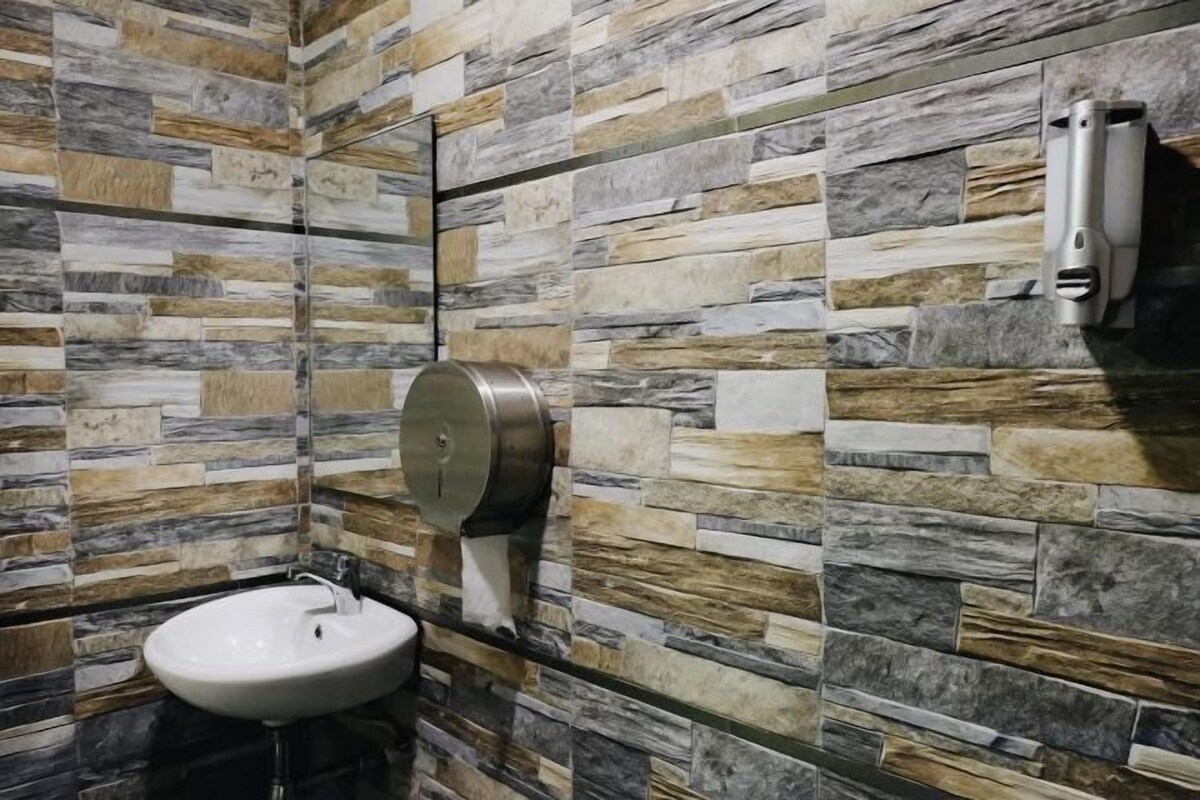 Une salle de bain avec un mur décoré d’un motif imitant la pierre, un lavabo et un distributeur de serviettes en papier.