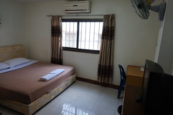 Habitación de hotel con cama, ventana con cortinas, equipo de aire acondicionado, escritorio con televisor y una silla.