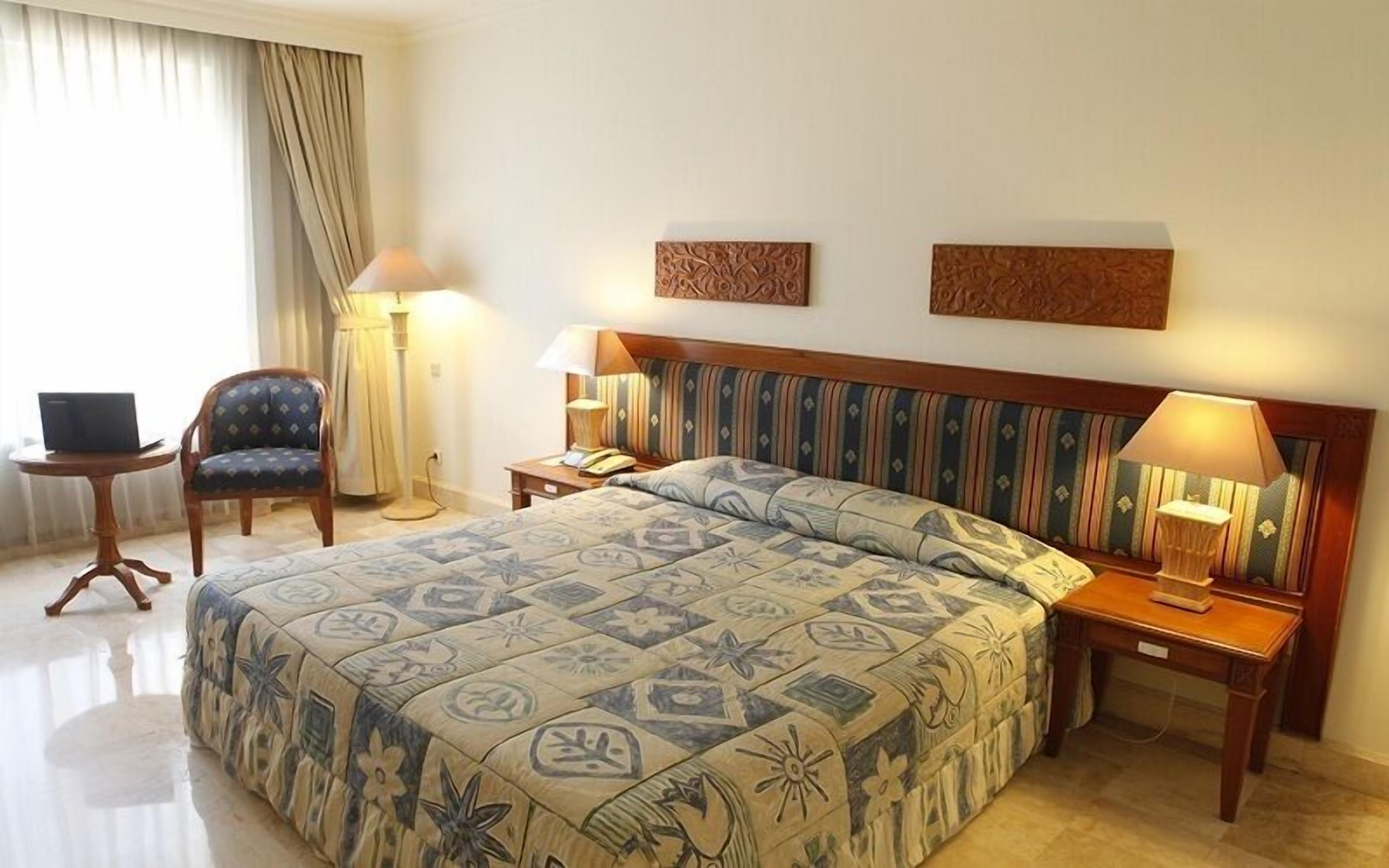 Une chambre d’hôtel avec un lit, une chaise, un bureau et deux lampes.