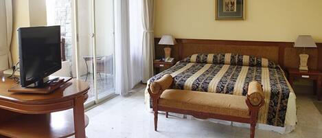 Une chambre d’hôtel avec un lit, un bureau avec un ordinateur, une chaise et une fenêtre avec des rideaux.