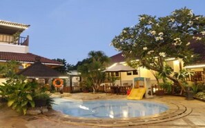A pool area with a slide, surrounded by palm trees and a building with a tiled roof. - Resor Tuban Tropis (Tuban)