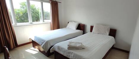 A hotel room with two beds, a window with curtains, and a view of greenery outside.