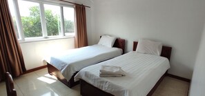 Camera d'albergo con due letti, una finestra con tende e vista su del verde all'esterno.