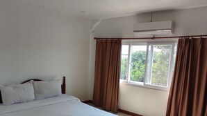 Un dormitorio con cama, cortinas, aire acondicionado y ventana con vista a follaje.