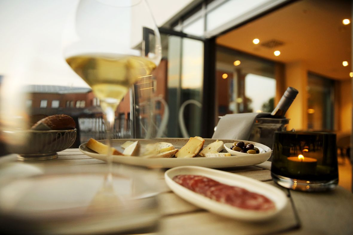 A dining table with plates of cheese, olives, and a small dish of red sauce, a candle, and a glass of wine.