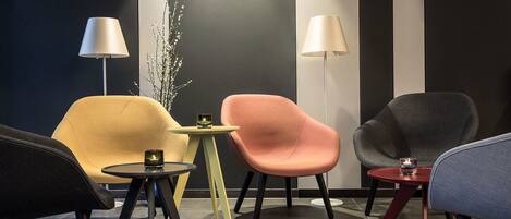A modern lounge area with four chairs and two small tables, each with a lamp.