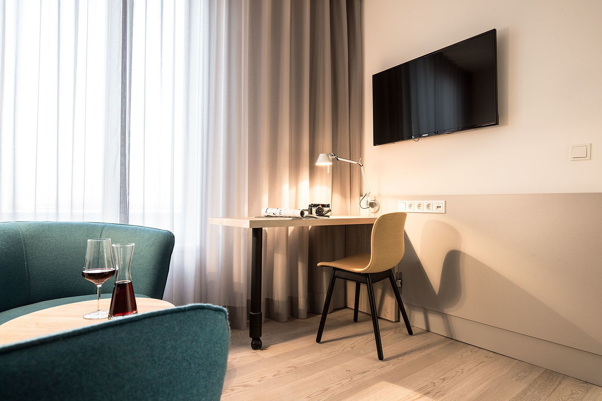 A modern hotel room with a wooden desk, a television mounted on the wall, a chair, and a couch.