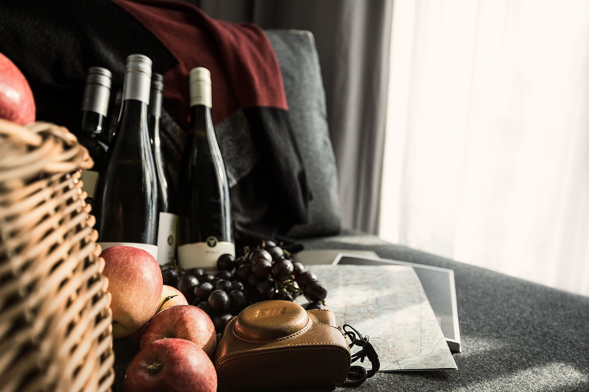 A wicker basket with apples, a wine bottle, and a camera on a table with a map.