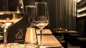 Une table de bar avec une pizza, deux verres de vin blanc et une bouteille de schnaps.