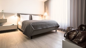 Une chambre d’hôtel moderne avec un lit, des tables de chevet, une lampe, un vase et un sac à main.