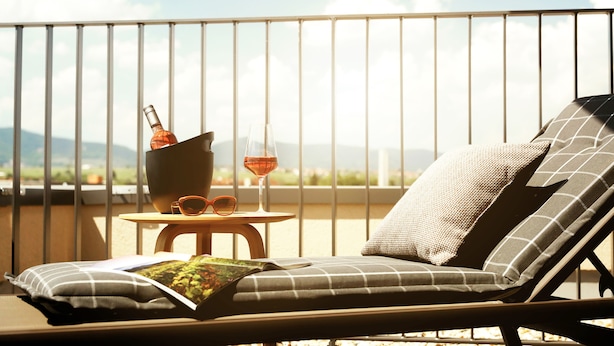 Un balcon avec un fauteuil de relaxation, une petite table sur laquelle se trouvent une bouteille, des verres et un magazine.