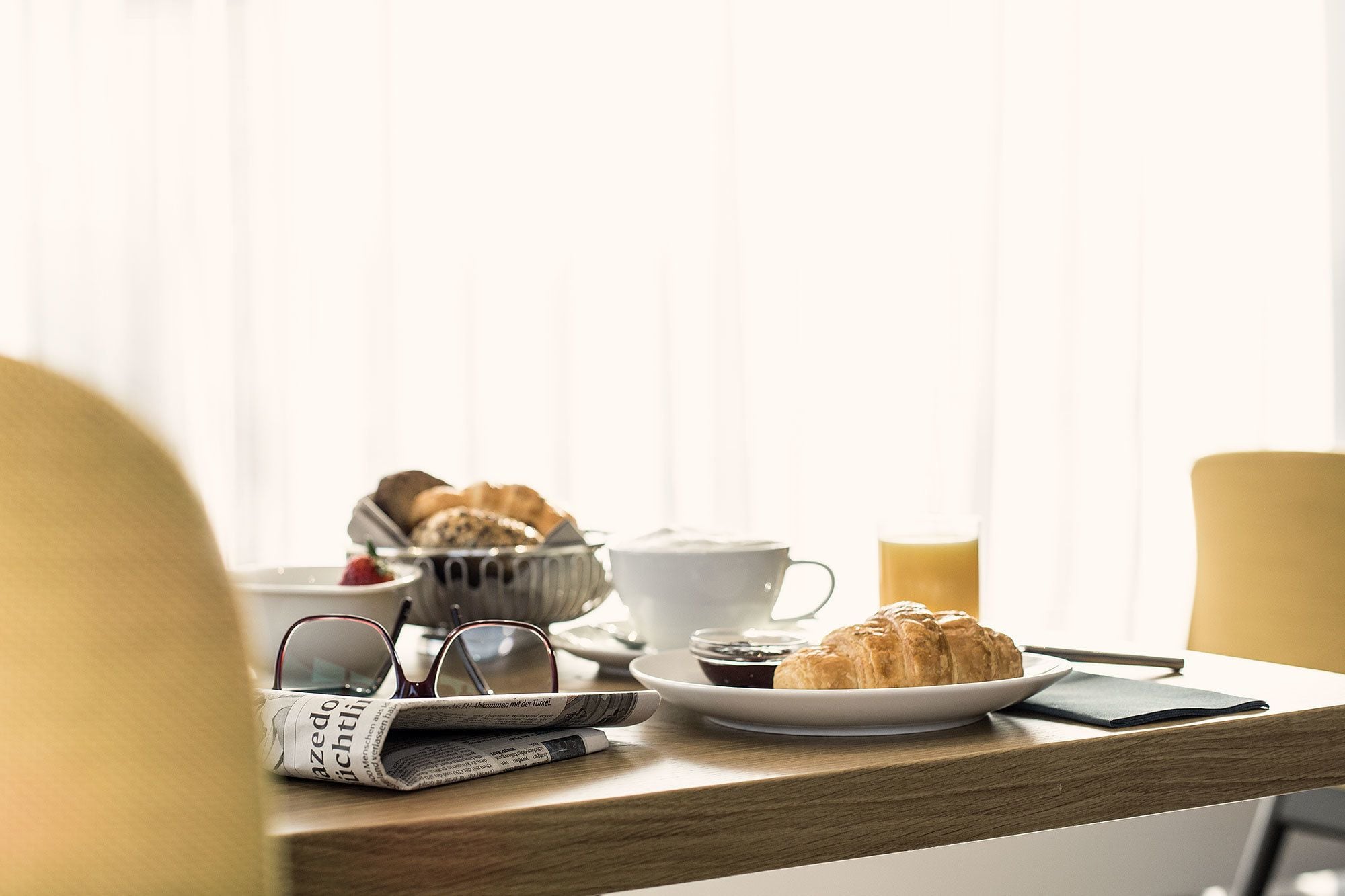 Desayuno con cruasanes, una taza de café y un periódico sobre una mesa de madera.