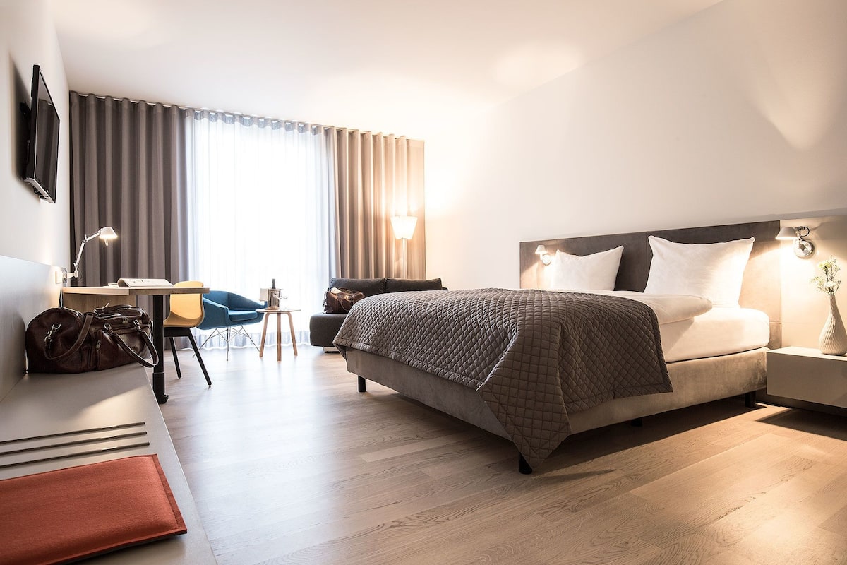 Una habitación de hotel moderna con una cama grande, un escritorio, una silla y un sofá.