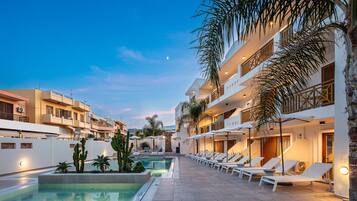 A poolside area with lounge chairs, a pool, and a building with balconies.